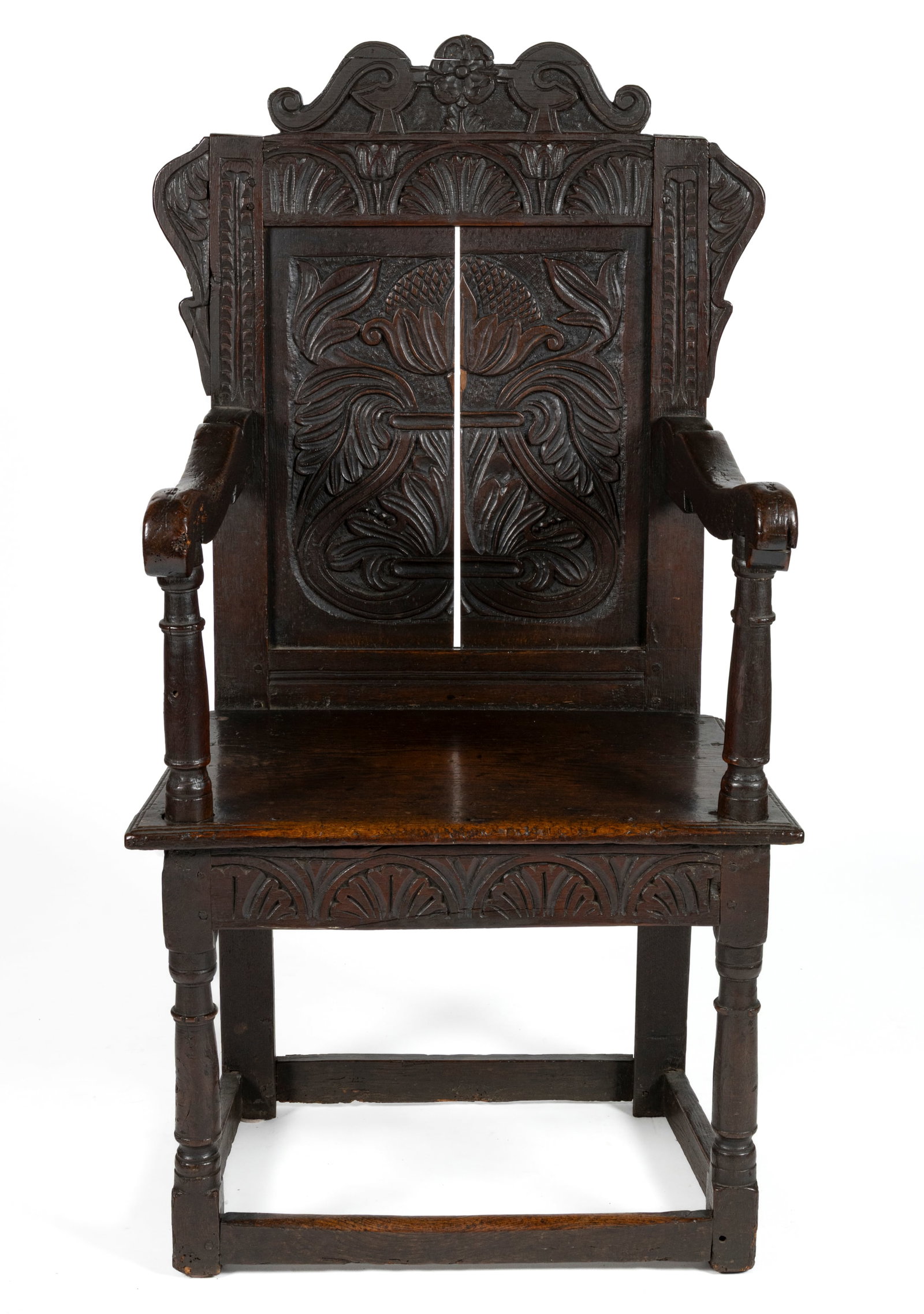 ENGLISH CARVED OAK WAINSCOT ARMCHAIR: ENGLISH CARVED OAK WAINSCOT ARMCHAIR, the shaped carved crest applied to the rectangular back over a trapezoidal seat, shaped scrolling arms and turned front posts joined to the square rear posts with