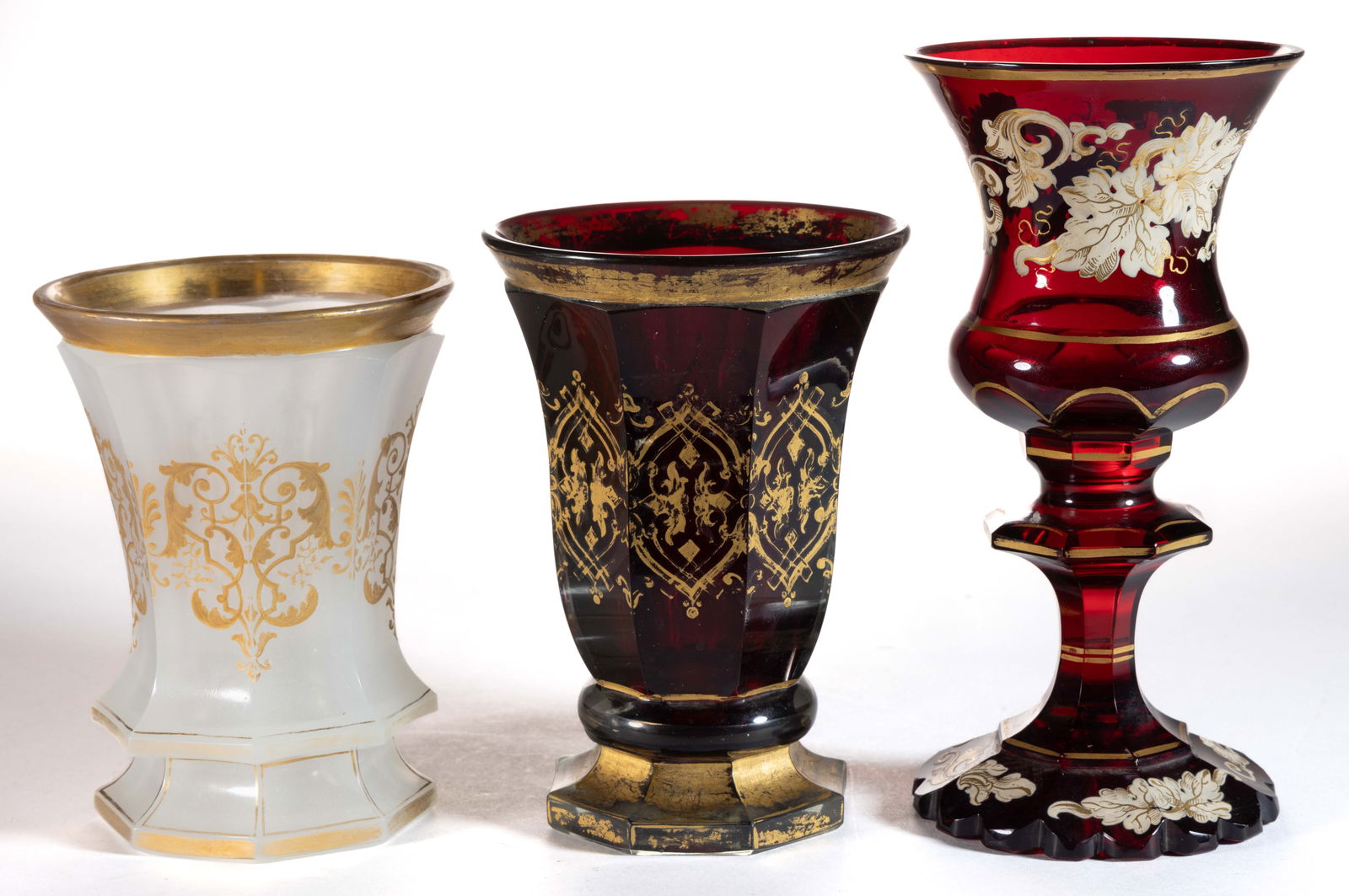 BOHEMIAN CUT AND GILT-DECORATED GLASS BEAKERS / DRINKING GLASSES, LOT OF THREE: BOHEMIAN CUT AND GILT-DECORATED GLASS BEAKERS / DRINKING GLASSES, LOT OF THREE, the smallest example in alabaster or clambroth glass featuring cut paneling on the thistle-form body with gilt leaf deco