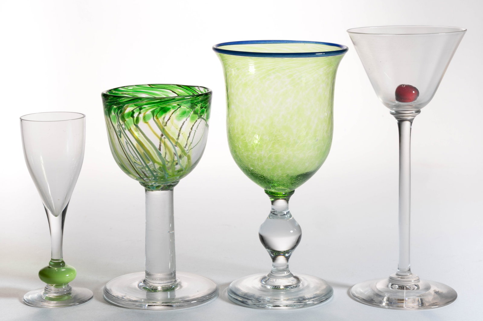 ASSORTED STUDIO ART GLASS DRINKING ARTICLES, LOT OF FOUR: ASSORTED STUDIO ART GLASS DRINKING ARTICLES, LOT OF FOUR, including a colorless A. Douglas Nash cordial with a green stem, a mottled green wine, and a martini glass with an interior red cherry. Variou