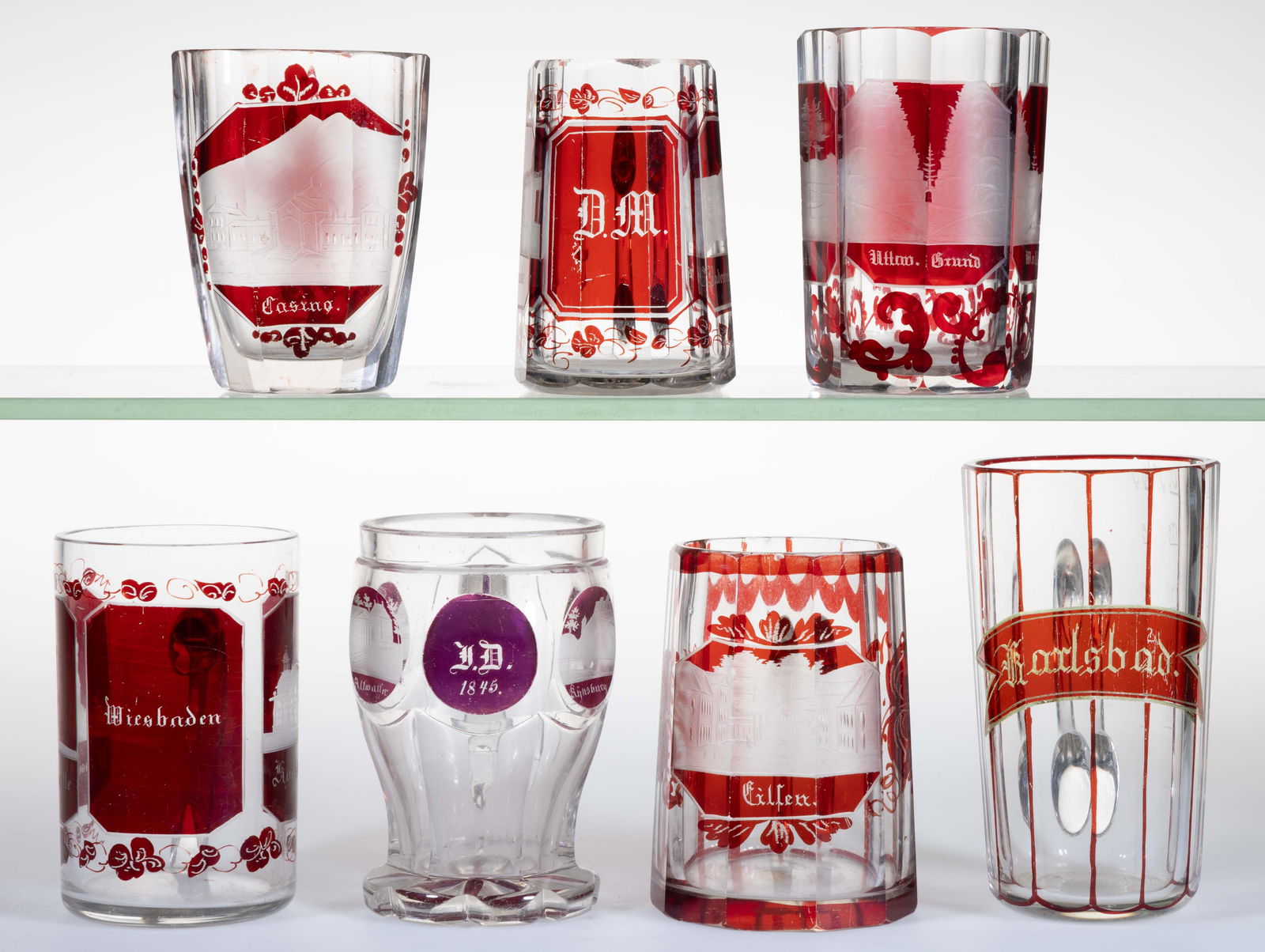 ASSORTED BOHEMIAN RUBY-STAINED AND ENGRAVED WITH SOUVENIR DRINKING ARTICLES, LOT OF SEVEN: ASSORTED BOHEMIAN RUBY-STAINED AND ENGRAVED WITH SOUVENIR DRINKING ARTICLES, LOT OF SEVEN, colorless with ruby stain, comprising of six tumblers and a flask-form tumbler/flask; five examples with appl
