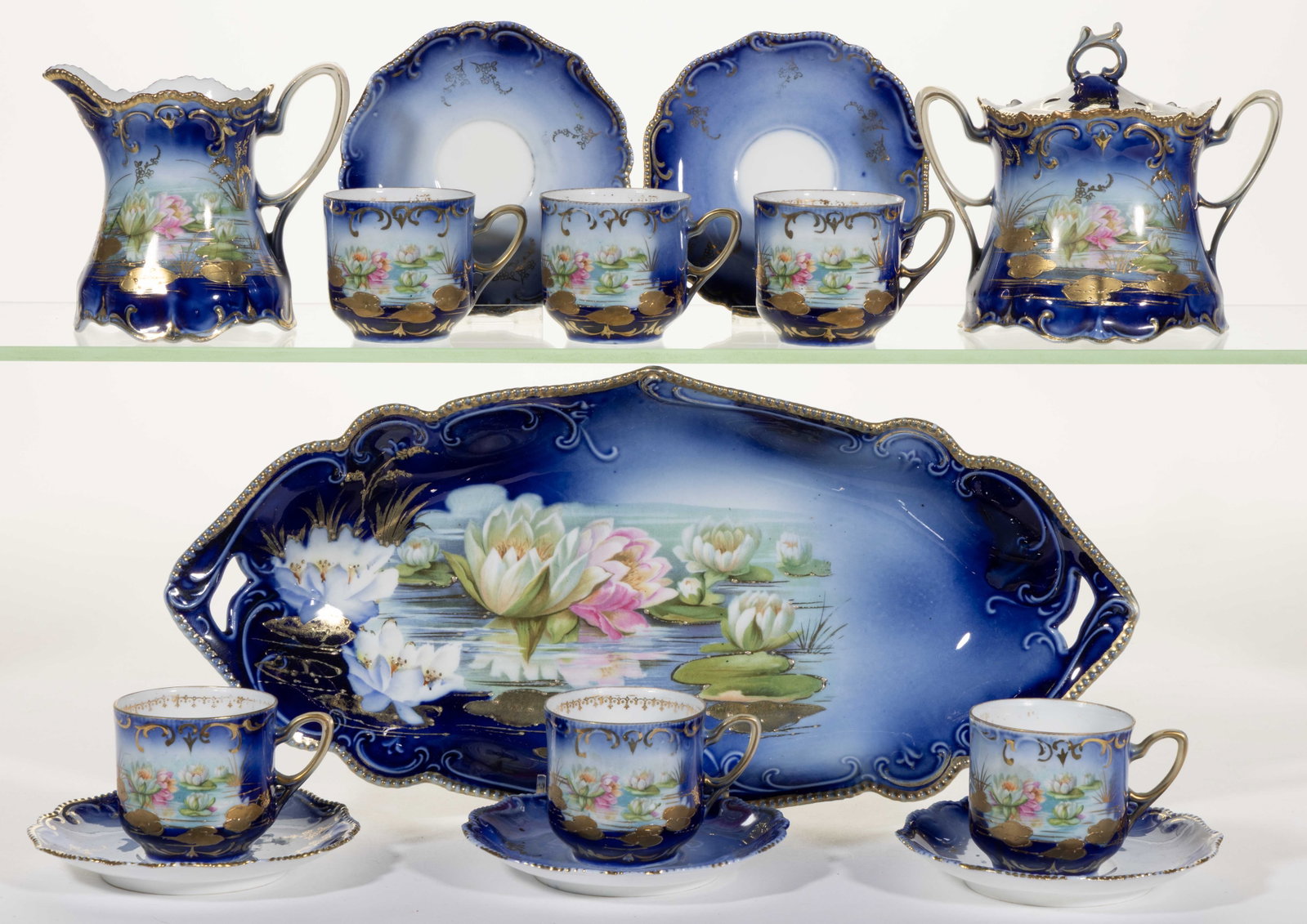R.S. PRUSSIA PORCELAIN COBALT-DECORATED WATER LILY MOTIF TEA AND TABLE ARTICLES, LOT OF 14: R.S. PRUSSIA PORCELAIN COBALT-DECORATED WATER LILY MOTIF TEA AND TABLE ARTICLES, LOT OF 14, each having polychrome transfer depicting reflective water lilies with gilt lily pads, comprising a sugar an