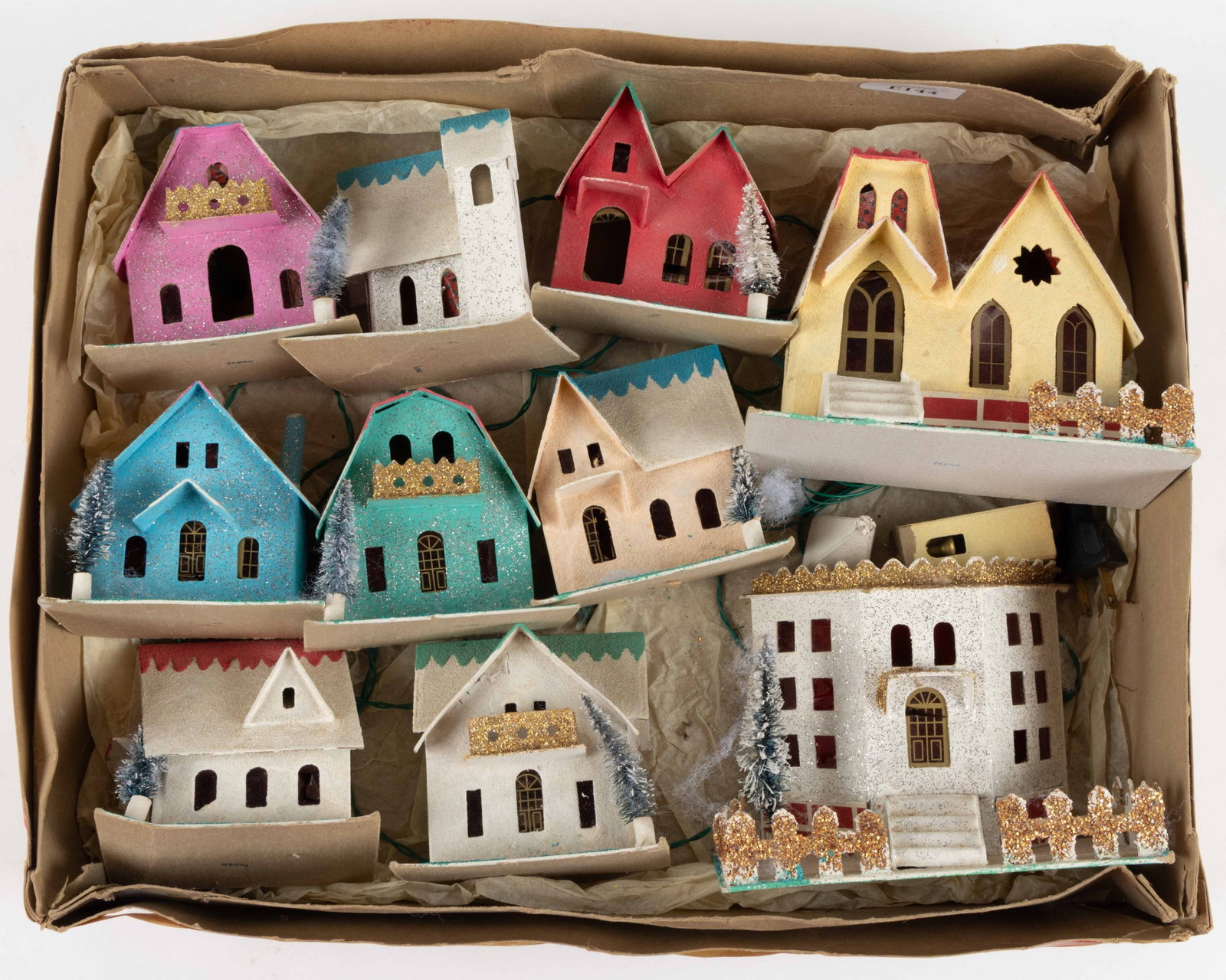 JAPANESE LIGHTED PUTZ HOUSE SET IN BOX: JAPANESE LIGHTED PUTZ HOUSE SET IN BOX, comprising eight houses, a larger structure, and a church, each with cellophane windows, and connected to the original light strand, each is stamped "JAPAN