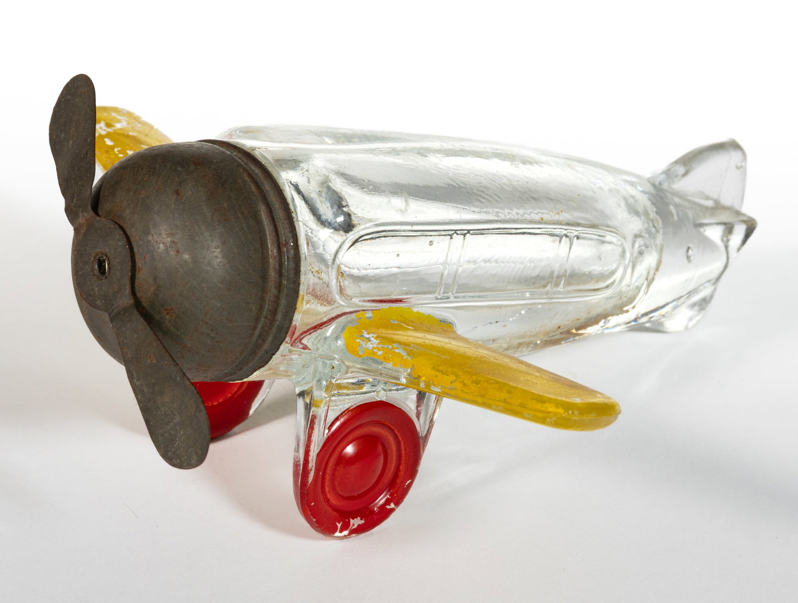 AIRPLANE WITH LEFT SIDE REAR DOOR FIGURAL PRESSED GLASS CANDY CONTAINER: AIRPLANE WITH LEFT SIDE REAR DOOR FIGURAL PRESSED GLASS CANDY CONTAINER, colorless with painted highlights including yellow wings and red wheels, pressed in the form of a plane with small wings and la