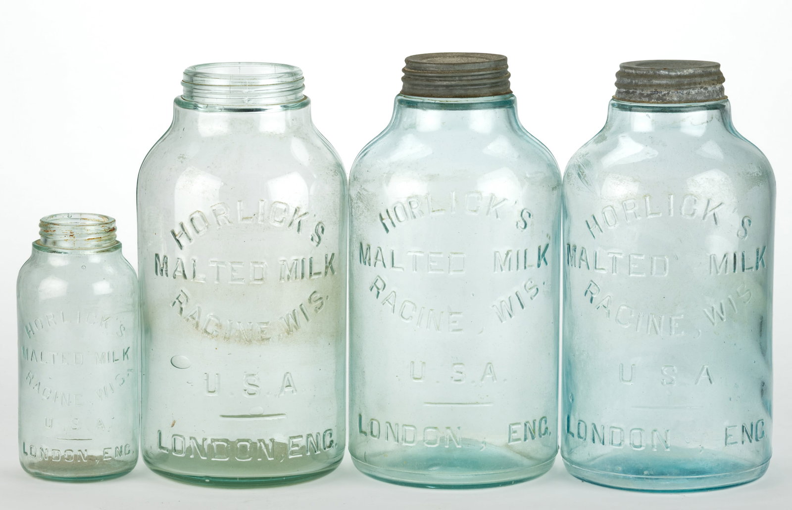 HORLICK'S MALTED MILK GLASS JARS, LOT OF FOUR: HORLICK'S MALTED MILK GLASS JARS, LOT OF FOUR, aquamarine, comprising one pint and three one-gallon examples, two with a lid, two embossed "I. G. Co. under the base. Fourth quarter 19th/early