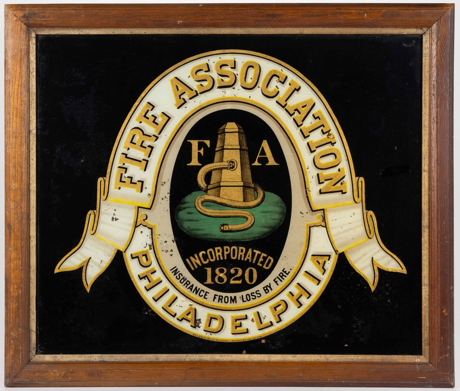 PHILADELPHIA FIRE ASSOCIATION REVERSE-PAINTED TRADE SIGN: PHILADELPHIA FIRE ASSOCIATION REVERSE-PAINTED TRADE SIGN, design featuring a fireman's pump and hose in oval reserve with a ribbon surround, housed under glass in an old frame. Fourth quarter 19th