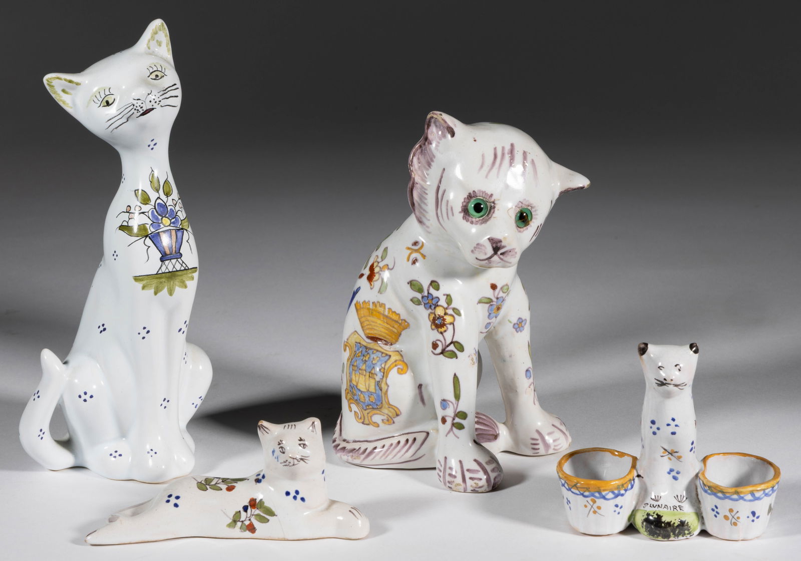 FRENCH FAIENCE TIN-GLAZED EARTHENWARE CAT FIGURES, LOT OF FOUR: FRENCH FAIENCE TIN-GLAZED EARTHENWARE CAT FIGURES, LOT OF FOUR, each having polychrome hand-painted floral decorations, comprising a recumbent cat with front paws crossed and three sitting examples in