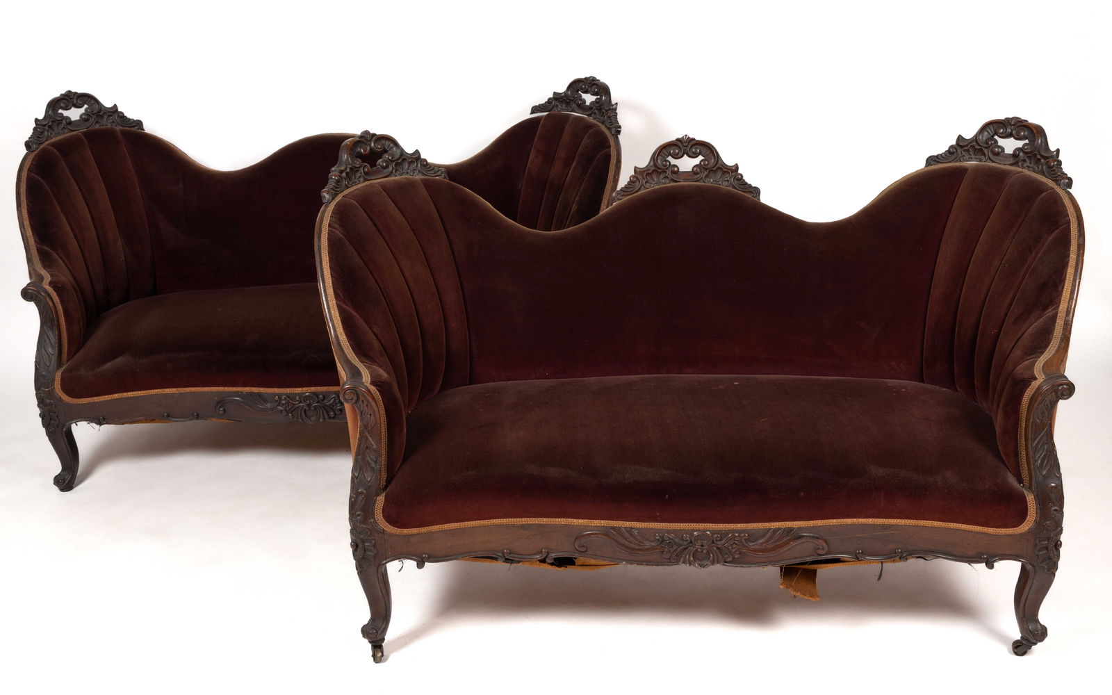 PAIR OF AMERICAN VICTORIAN CARVED MAHOGANY SOFAS / SETTEES: PAIR OF AMERICAN VICTORIAN CARVED MAHOGANY SOFAS / SETTEES, the shaped back with applied carved elements over a shaped seat, the whole raised on carved cabriole legs. Each with an older velvet upholst