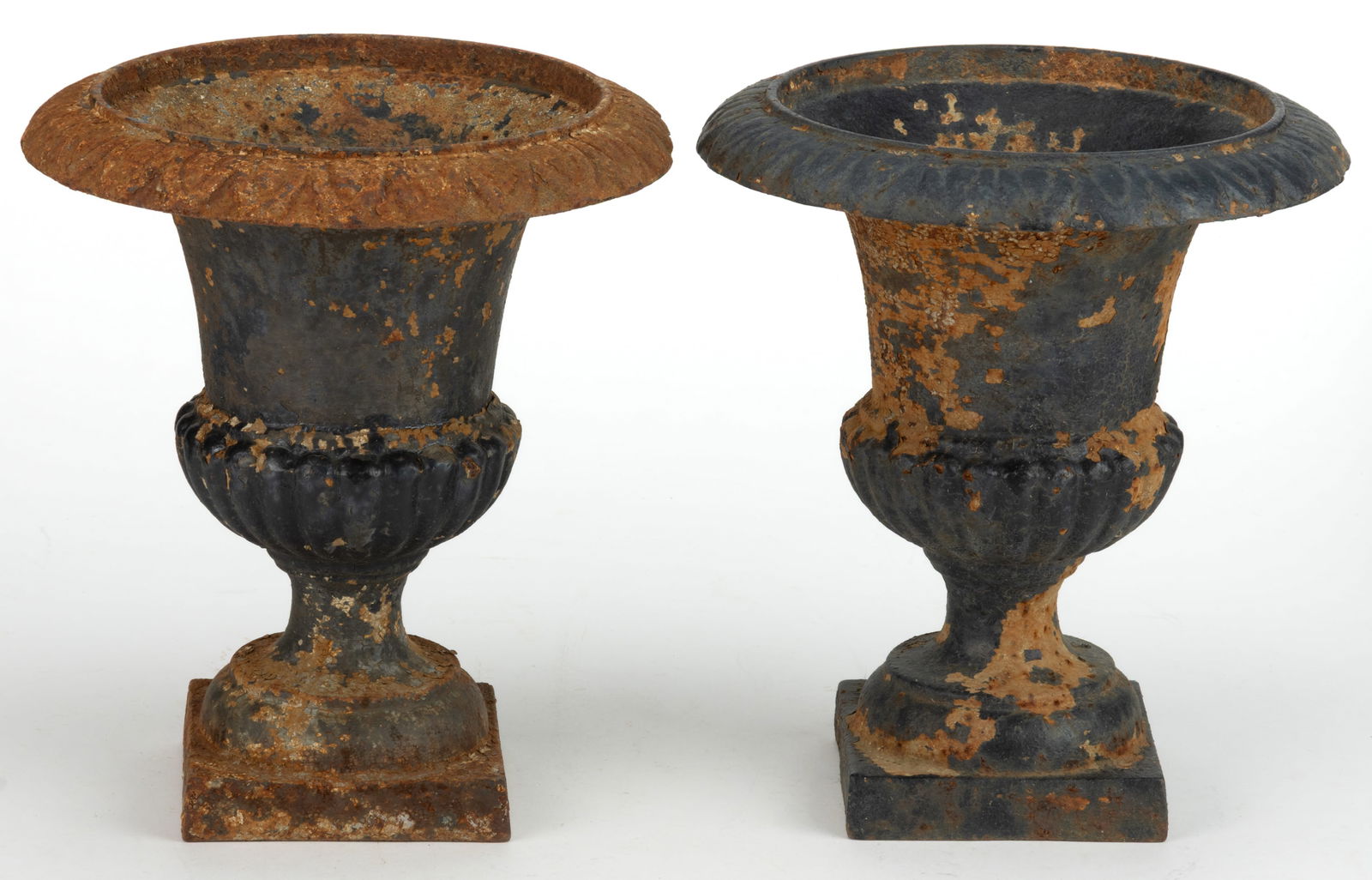 PAIR OF AMERICAN DIMINUTIVE CAST-IRON GARDEN URNS: PAIR OF AMERICAN DIMINUTIVE CAST-IRON GARDEN URNS, each with a flared upper edge which tapered to a gadrooned base, the whole resting on a round socle and square platform. Each retains remnants of an