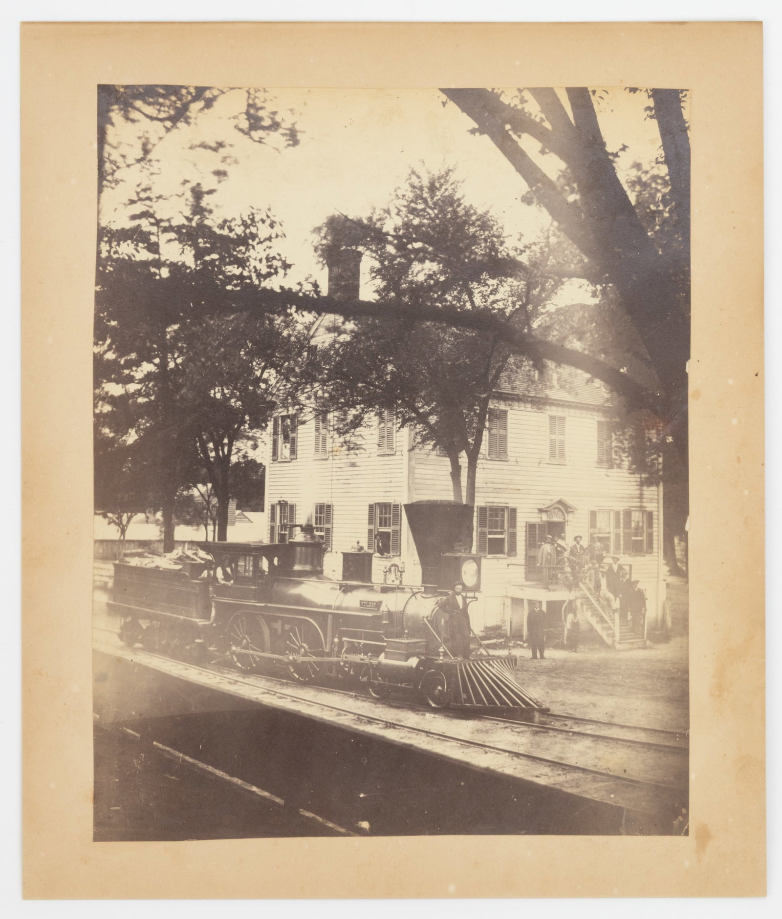 NEW BERN, NORTH CAROLINA STEAM LOCOMOTIVE PHOTOGRAPH: NEW BERN, NORTH CAROLINA STEAM LOCOMOTIVE PHOTOGRAPH, albumen print on studio cardstock, depicting a Vulcan engine and tender full of wood stopped in front of a large two-story house with men standing
