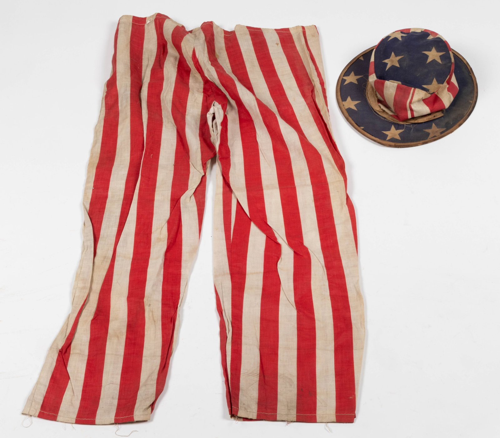 ANTIQUE AMERICAN PRINTED COTTON PATRIOTIC COSTUME PARADE ARTICLES, LOT OF TWO: ANTIQUE AMERICAN PRINTED COTTON PATRIOTIC COSTUME PARADE ARTICLES, LOT OF TWO, comprising a hat with stars, stripes, and wire rim, and a pair of striped trousers. Late 19th/early 20th century. Tr