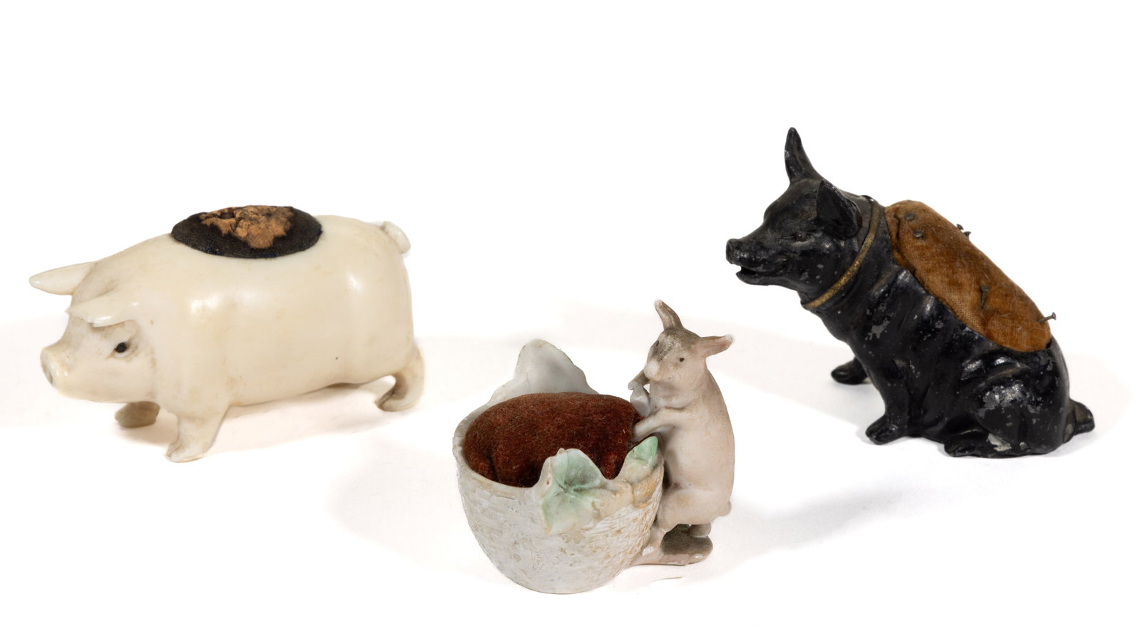 ASSORTED MATERIALS FIGURAL PIG NEEDLEWORKING / SEWING PINCUSHIONS, LOT OF THREE: ASSORTED MATERIALS FIGURAL PIG NEEDLEWORKING / SEWING PINCUSHIONS, LOT OF THREE, comprising a bone standing example with fabric-covered cork pincushion, painted black eyes; a black-painted aluminum/sp
