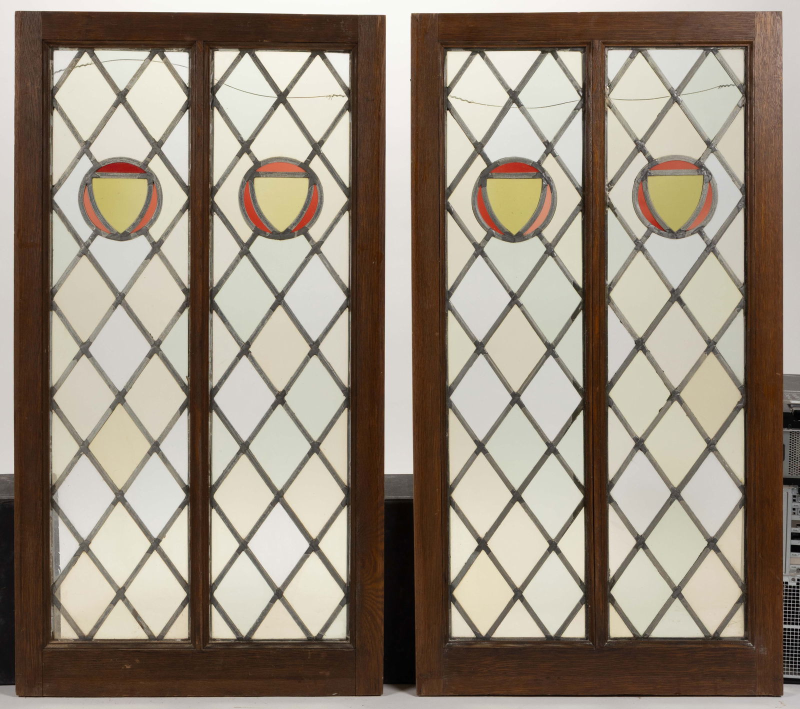 PAIR OF ENGLISH OR AMERICAN ARTS AND CRAFTS STAINED- AND LEADED-GLASS WINDOWS: PAIR OF ENGLISH OR AMERICAN ARTS AND CRAFTS STAINED- AND LEADED-GLASS WINDOWS, each having two slender panels with a diamond/lattice patterned ground with a central shield in a circular reserve. Each