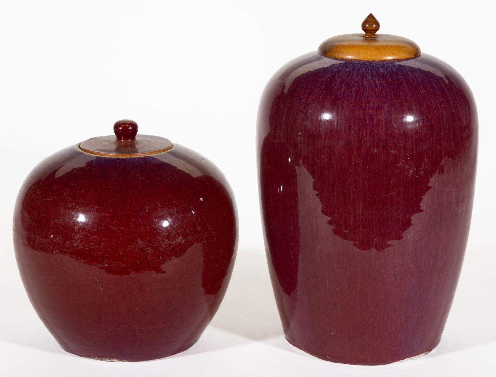 CHINESE OXBLOOD / SANG DE BOEUF PORCELAIN COVERED JARS, LOT OF TWO: CHINESE OXBLOOD / SANG DE BOEUF PORCELAIN COVERED JARS, LOT OF TWO, each having mottled purplish glaze to top, comprising one ginger example with porcelain cover and one tall example with wooden