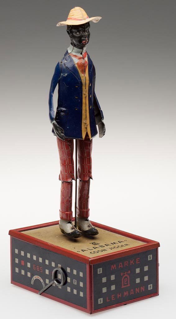 BLACK AMERICANA LEHMANN "OH MY ALABAMA COON JIGGER" WIN: BLACK AMERICANA LEHMANN "OH MY ALABAMA COON JIGGER" WIND-UP TIN TOY, with articulated arms and legs, dark blue jacket and striped red pants, tan-top platform variation with red, white and blue sides,
