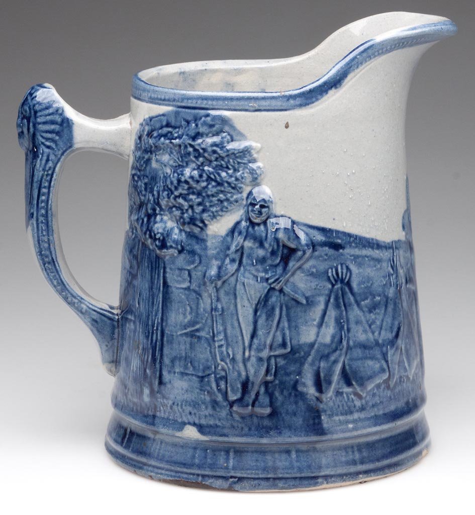 INDIAN SCENE SALT-GLAZED STONEWARE PITCHER: INDIAN SCENE SALT-GLAZED STONEWARE PITCHER, blue and grey, embossed full-round scene of an Indian camp with figures, teepees and cactus, chief mask on handle, ink stamped "Manufactured By / Belknap Hd