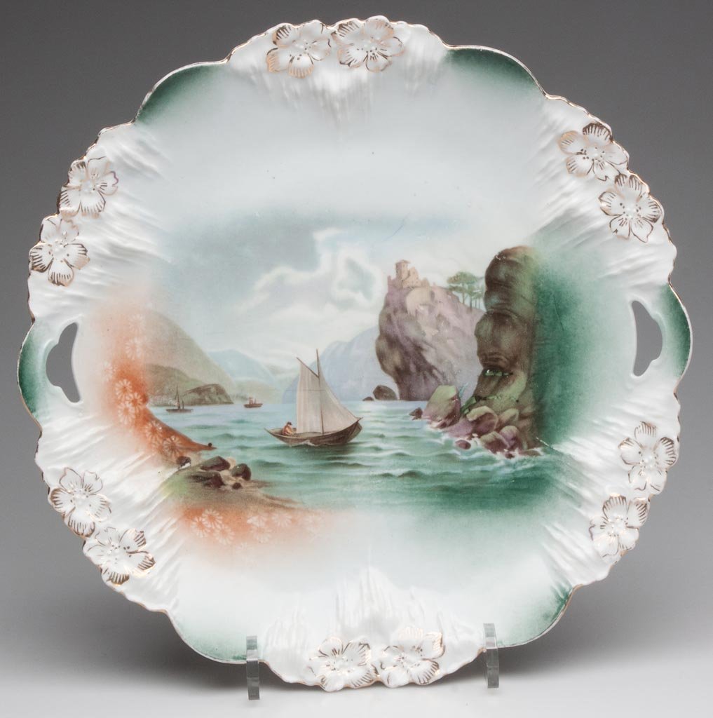 R. S. PRUSSIA SCENIC CAKE PLATE: R. S. PRUSSIA SCENIC CAKE PLATE, "Icicle" mold 7 transfer-printed with Man in Mountain, sailboat and castle on cliff, red and green wreath-and-star mark. Late 19th/early 20th century. 10 1/4" D. Prove