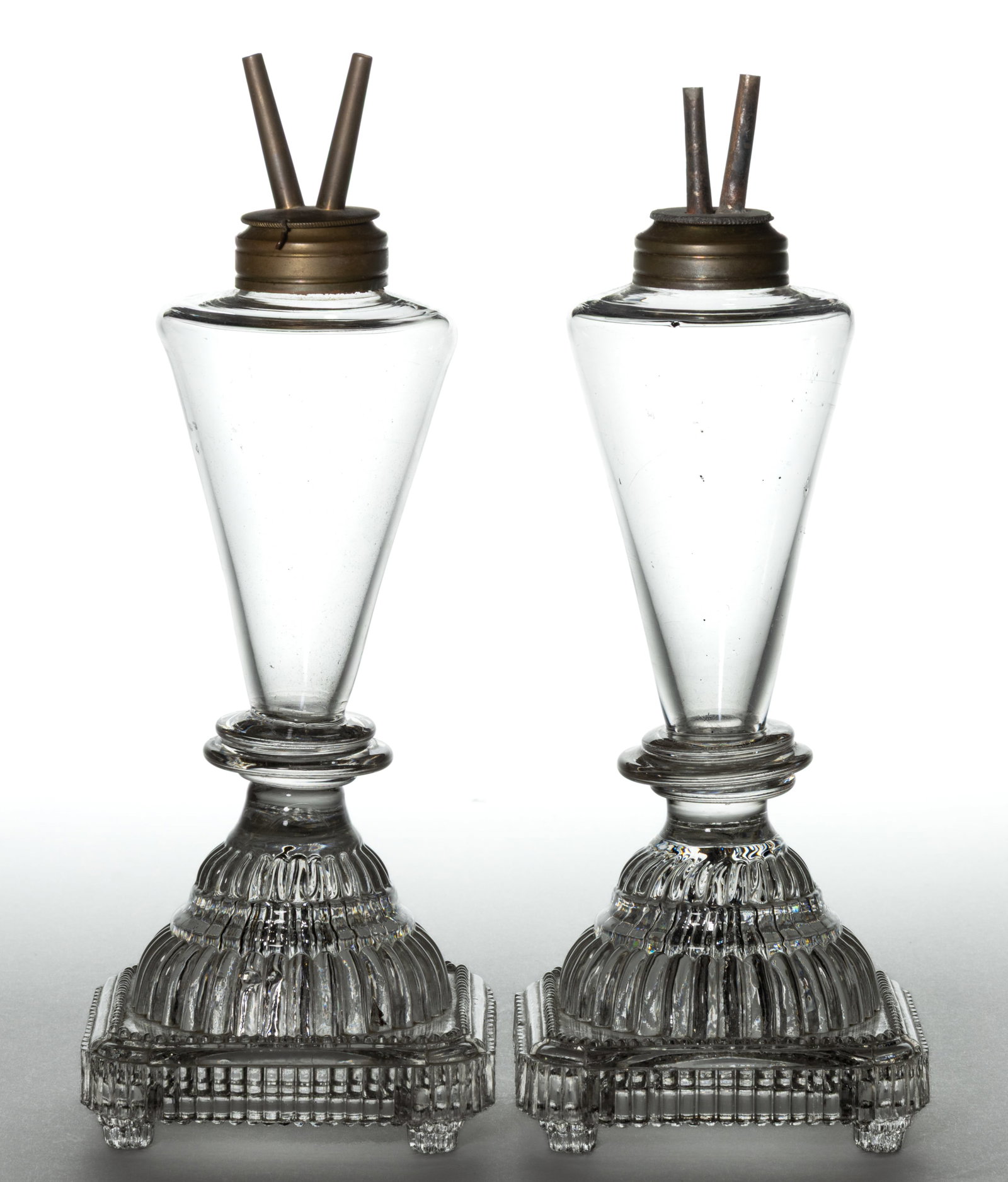 FREE-BLOWN FONT WHALE OIL / FLUID STAND LAMPS, PAIR: FREE-BLOWN FONT WHALE OIL / FLUID STAND LAMPS, PAIR, colorless, conical-form fonts, pressed ribbed base with double step stem, square-form foot with beading to the top and ribs to the sides, 