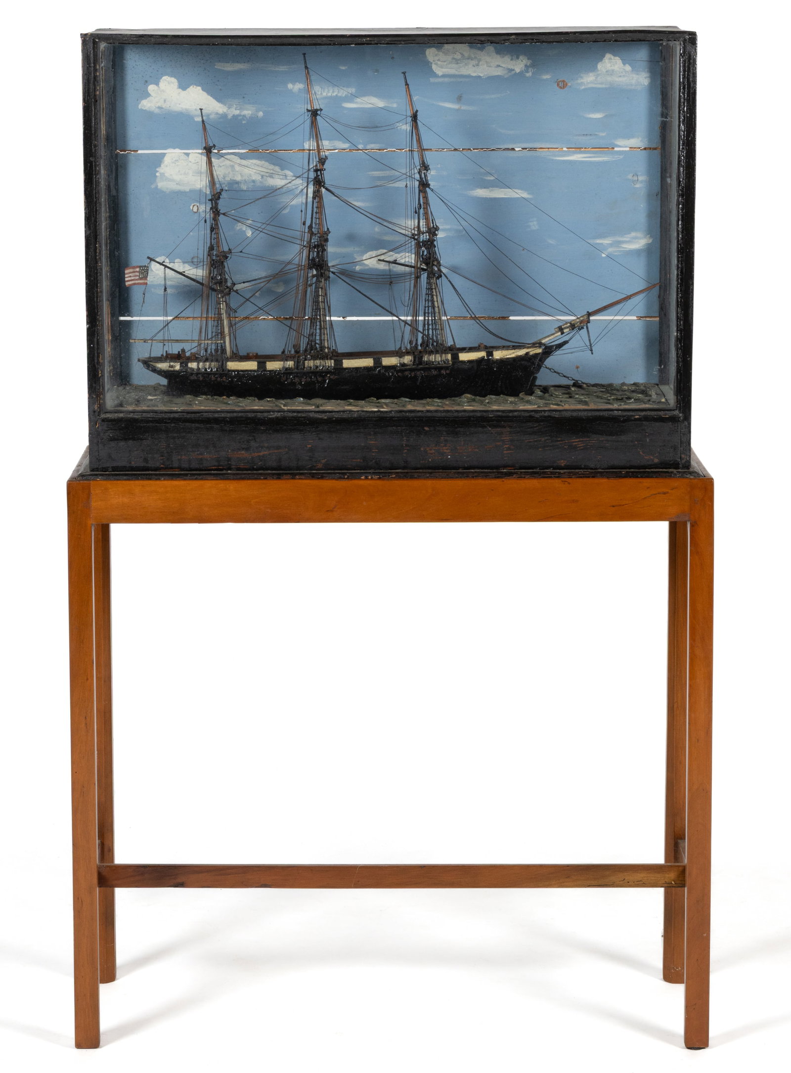 NEW ENGLAND FOLK ART CARVED AND PAINTED WOODEN SHIP MODEL IN CASE: NEW ENGLAND FOLK ART CARVED AND PAINTED WOODEN SHIP MODEL IN CASE, the pine case features glazed panels on the front and ends, the rear painted with a cloudy sky, the three-mast ship flies an American