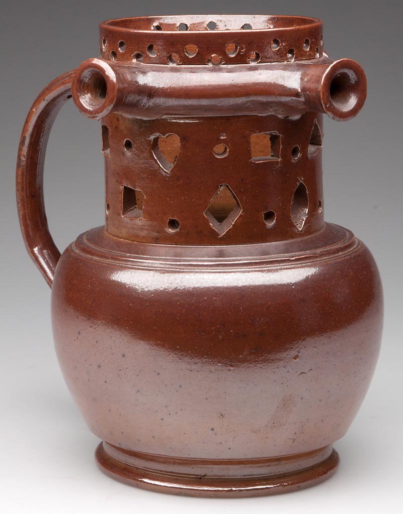 ENGLISH STONEWARE PUZZLE JUG: ENGLISH STONEWARE PUZZLE JUG, the salt-glazed brown stoneware body with narrow perforated neck, wide collar ring with three nozzles; above a wide-panelled lower neck reticulated with squares, dots, di