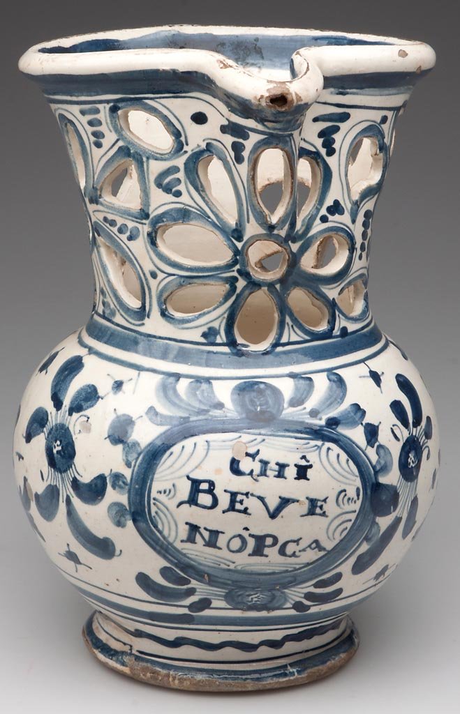 SAVONA (ITALY) FAIENCE PUZZLE JUG: SAVONA (ITALY) FAIENCE PUZZLE JUG, with a wide ovate mouth incorporating the puzzle jug collar, the central pinched spout with hole above a very wide neck deeply-cut with large flowers and geometric s
