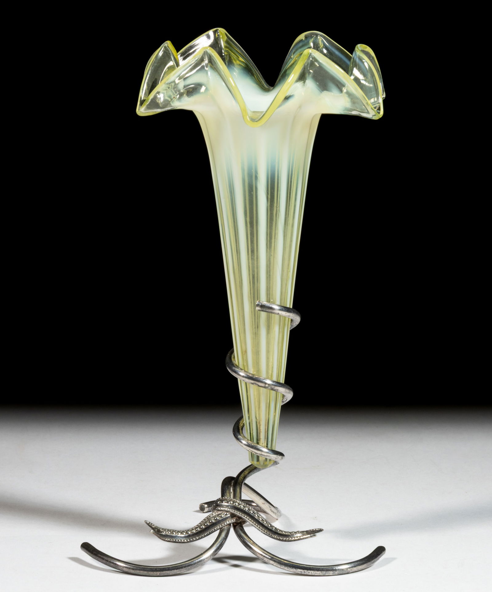 VICTORIAN VASELINE OPALESCENT LILY / TRUMPET VASE: VICTORIAN VASELINE OPALESCENT LILY / TRUMPET VASE, reacts under black light, rib-optic with folded rim, fitted in an unmarked silver-plate stand. Late 19th/early 20th century. 8 1/8" HOA, 4 1/4&q