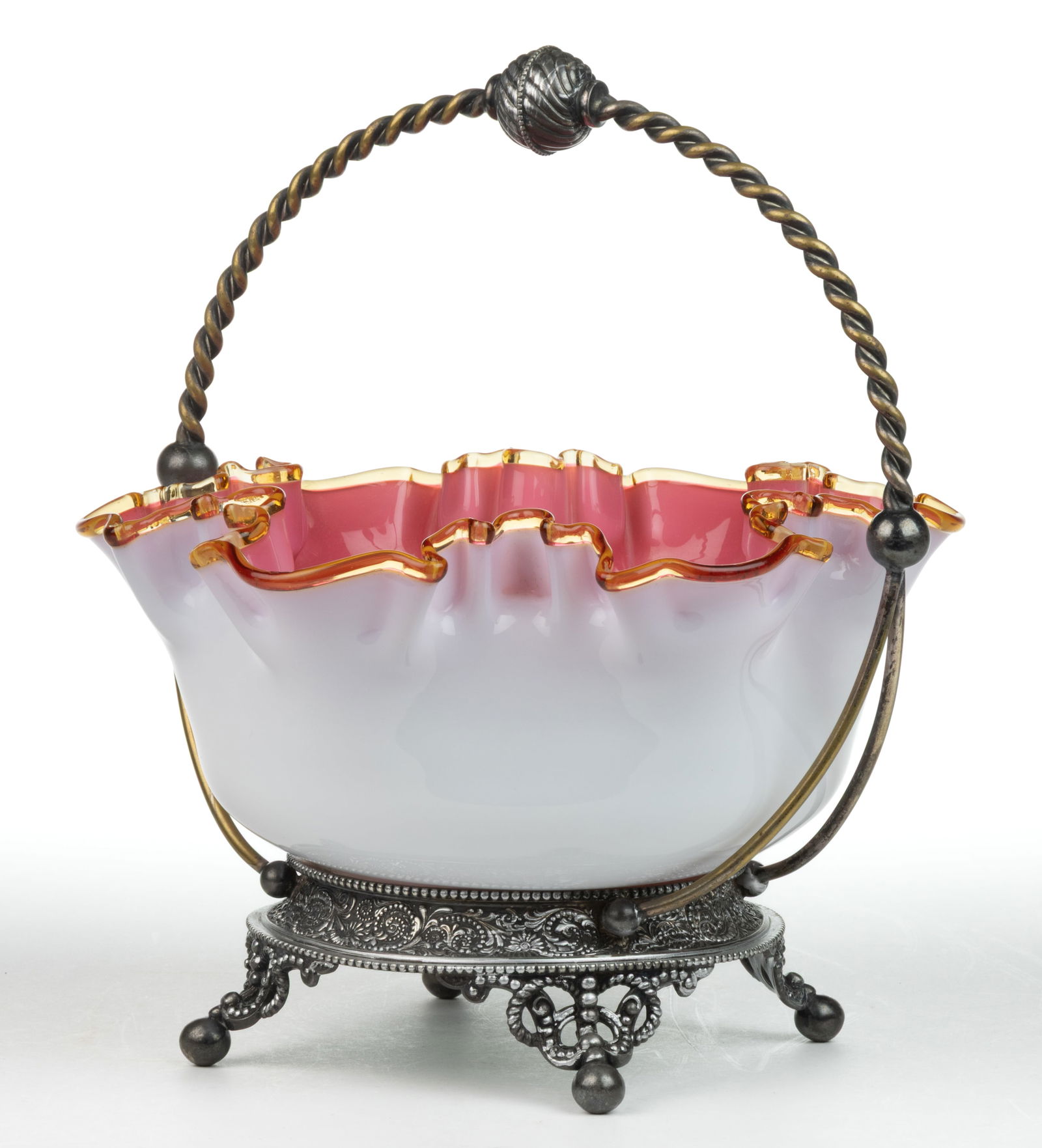 VICTORIAN CASED GLASS BRIDE'S BASKET: VICTORIAN CASED GLASS BRIDE'S BASKET, opaque white to opaque pink, with an applied amber ruffled-rim, polished pontil mark, fitted into a quadruple-plate stand stamped for "WILCOX S