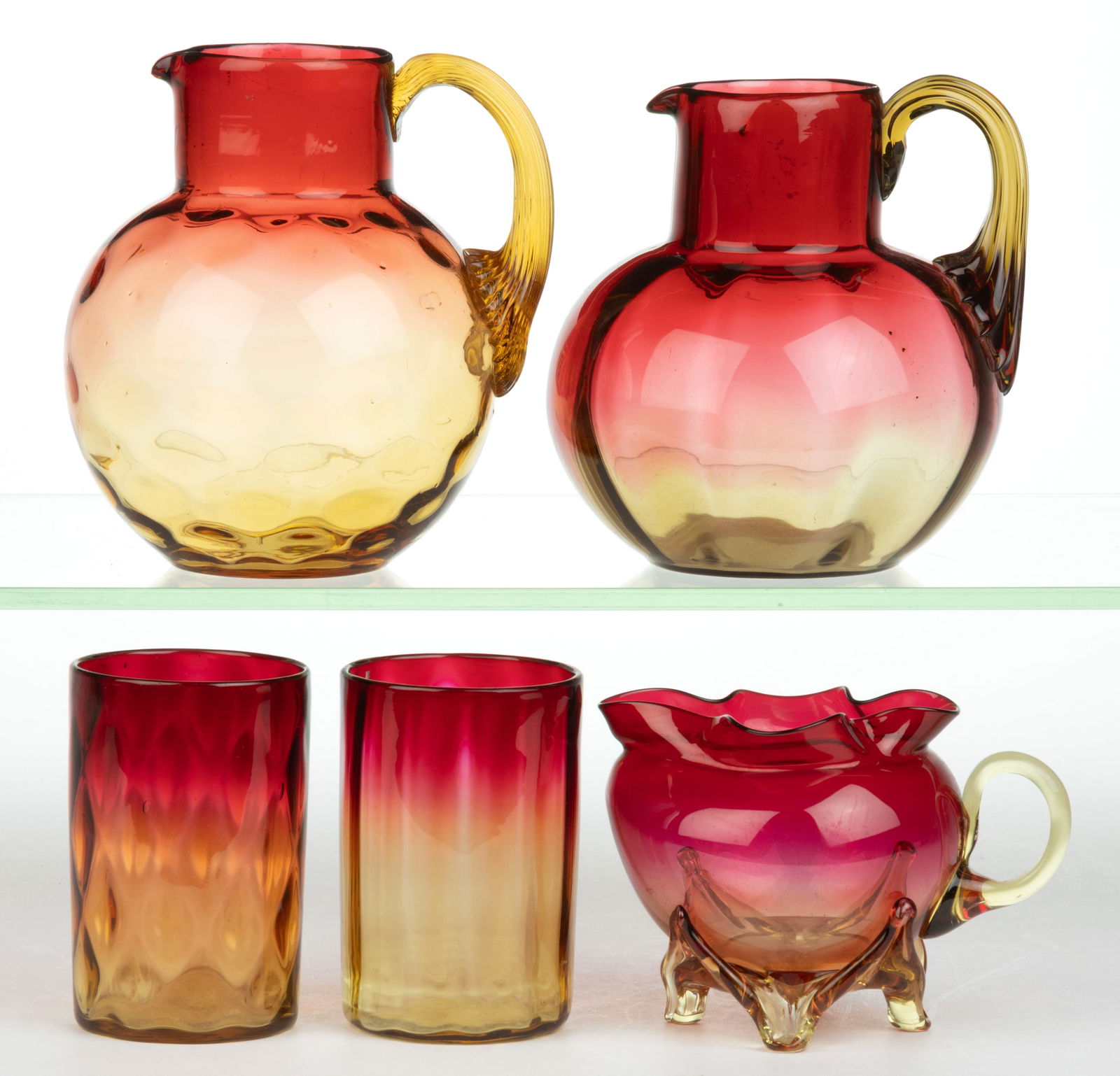 ASSORTED AMBERINA GLASS ARTICLES, LOT OF FIVE: ASSORTED AMBERINA GLASS ARTICLES, LOT OF FIVE, comprising two bulbous form pitchers each with applied reeded handle, two tumblers, and a creamer with applied handle and feet. Various makers. Four