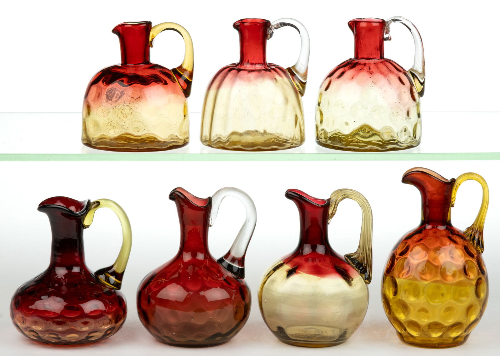 ASSORTED OPTIC PATTERN AMBERINA CRUETS, LOT OF SEVEN: ASSORTED OPTIC PATTERN AMBERINA CRUETS, LOT OF SEVEN, comprising one Rib, one Rib and Diamond Panel, and five Dot, each with an applied handle and polished pontil mark, lacking stoppers. Fourth quarte