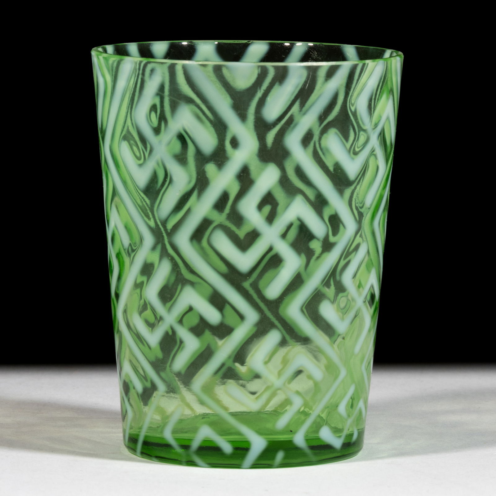 SWASTIKA TUMBLER: SWASTIKA TUMBLER, green opalescent, factory-polished rim, pattern introduced in 1904. Dugan Glass Company. Circa 1904. 3 7/8" H.Literature: Parallels Heacock/Elmore - Opalescent Glass From A-Z, p