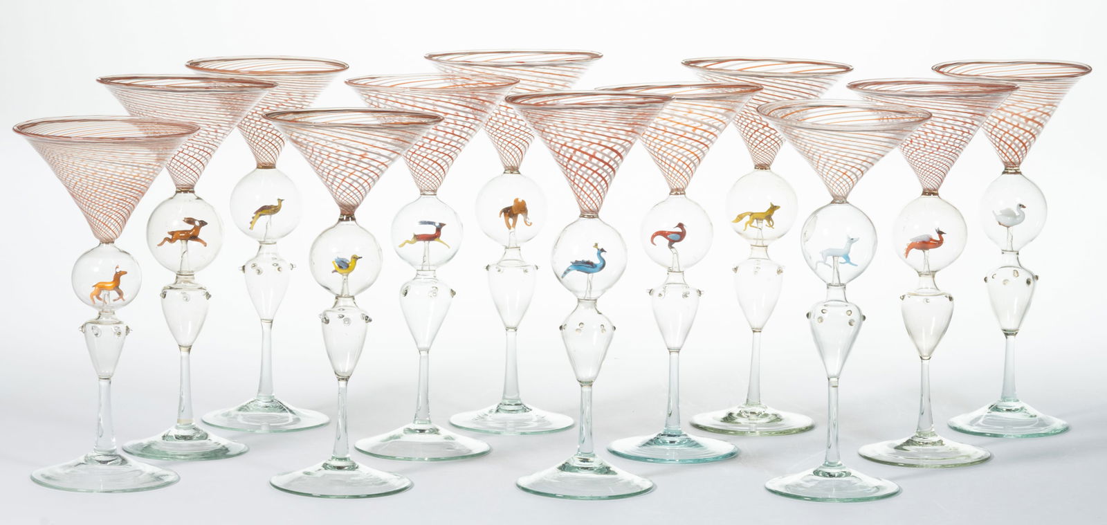 GERMAN ART GLASS BIMINI-TYPE MARTINI / COCKTAIL GLASSES, ASSEMBLED SET OF 12: GERMAN ART GLASS BIMINI-TYPE MARTINI / COCKTAIL GLASSES, ASSEMBLED SET OF 12, red and white swirl on colorless, each having a lampwork figure in the stem. Figures include a hare, a peacock, a pheasant