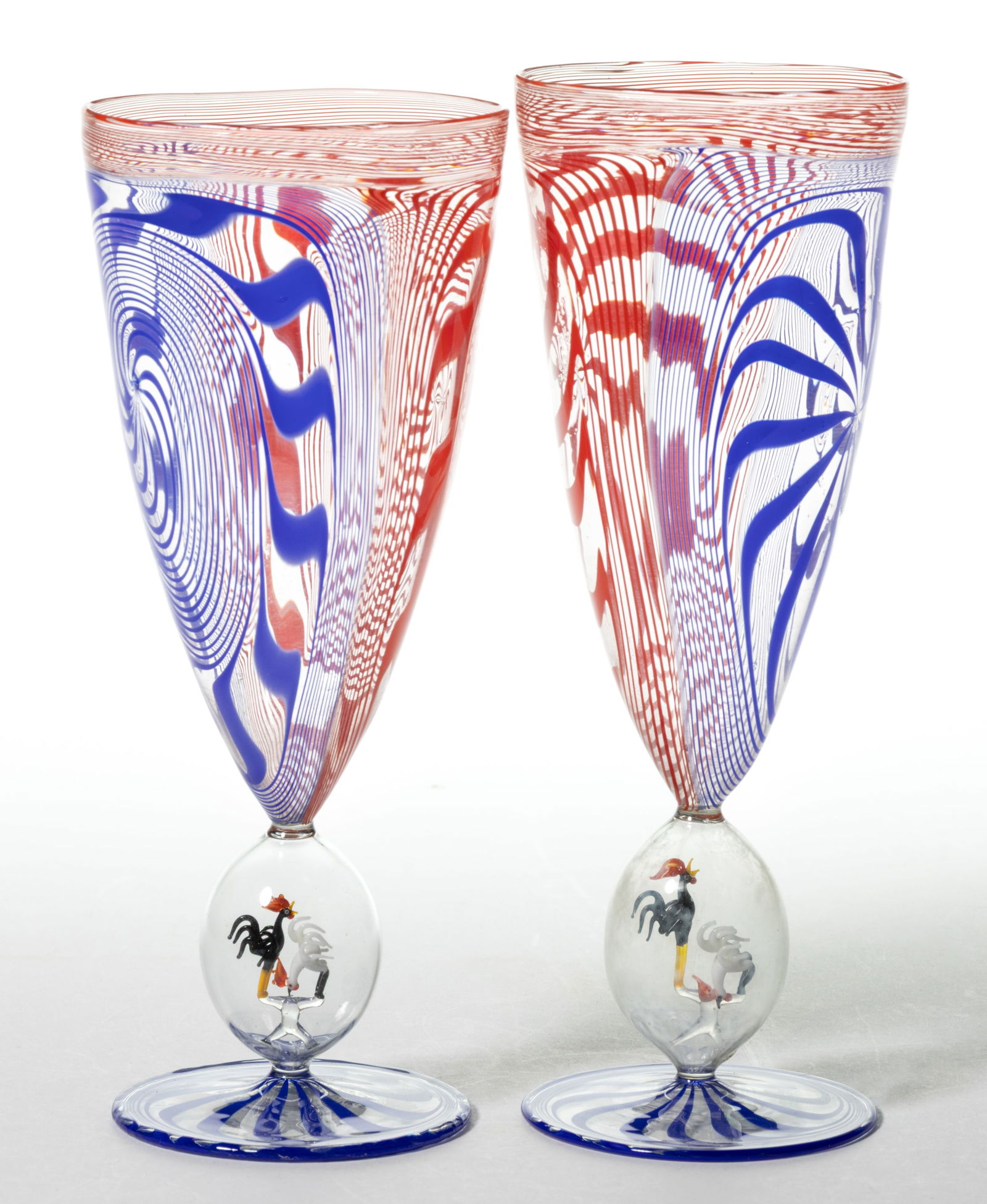 GERMAN ART GLASS BIMINI-TYPE ALE / COCKTAIL GLASSES, PAIR: GERMAN ART GLASS BIMINI-TYPE ALE / COCKTAIL GLASSES, PAIR, red and blue stylized swirl on colorless, each having a pair of lampwork fighting cocks in the stem. First half 20th century. 7 5/8"