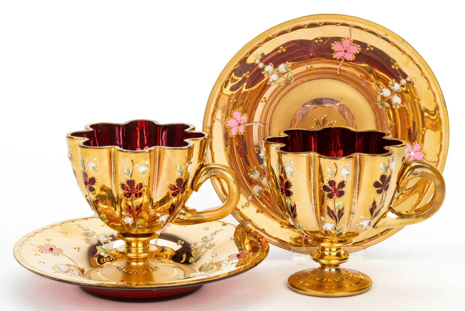 BOHEMIAN MOSER-STYLE CUP AND SAUCER, PAIR: BOHEMIAN MOSER-STYLE CUP AND SAUCER, PAIR, comprising a pair of cranberry footed cups with high relief floral decoration on overall gilt ground, each with applied handle and colorless