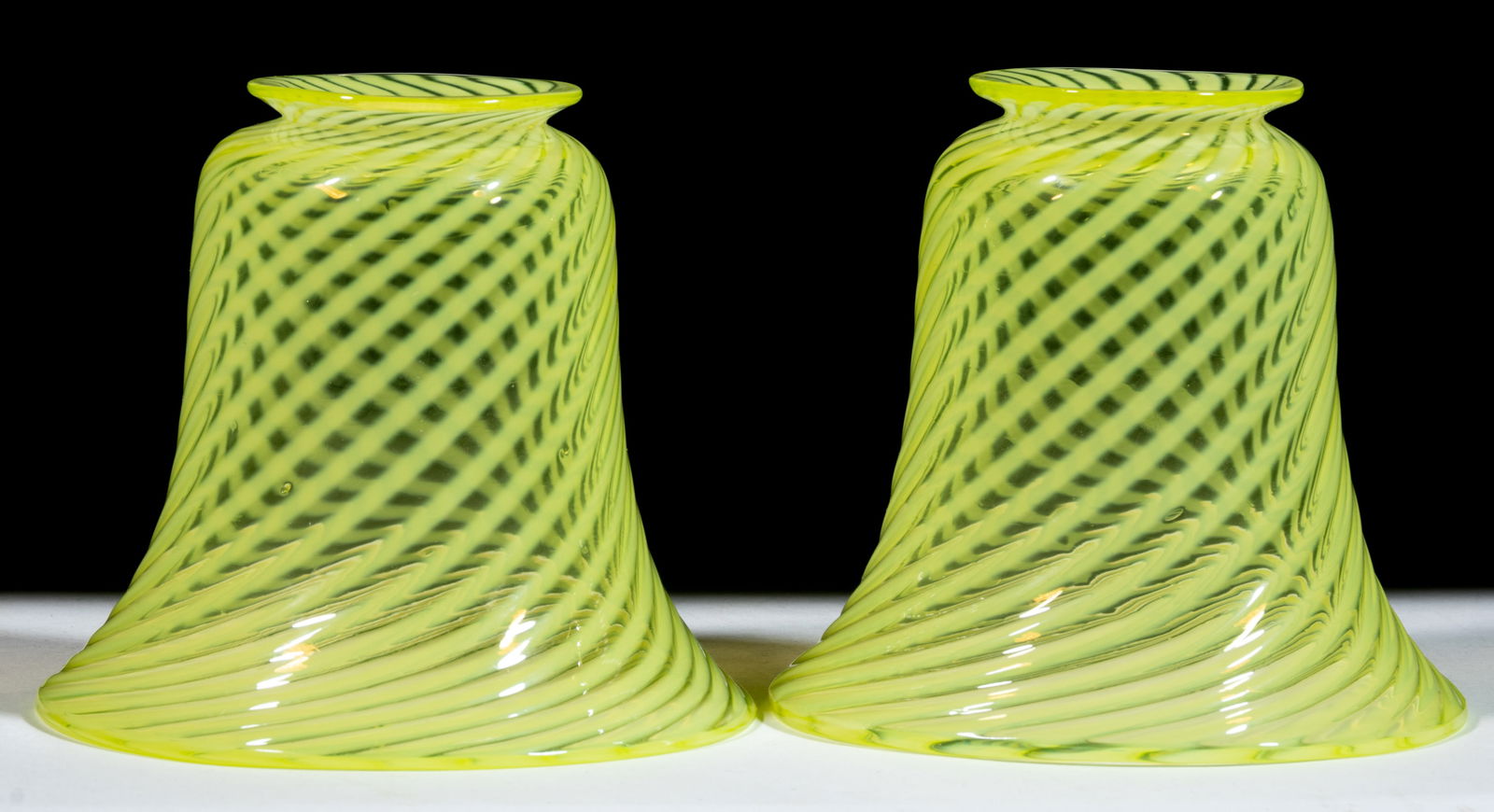 VASELINE OPALESCENT SWIRL ELECTRIC LAMP SHADES, PAIR: VASELINE OPALESCENT SWIRL ELECTRIC LAMP SHADES, PAIR, Vaseline (reacts under blacklight), each in bell-form with swirled opalescent decoration. First quarter 20th century. 4 1/4" HOA, 5