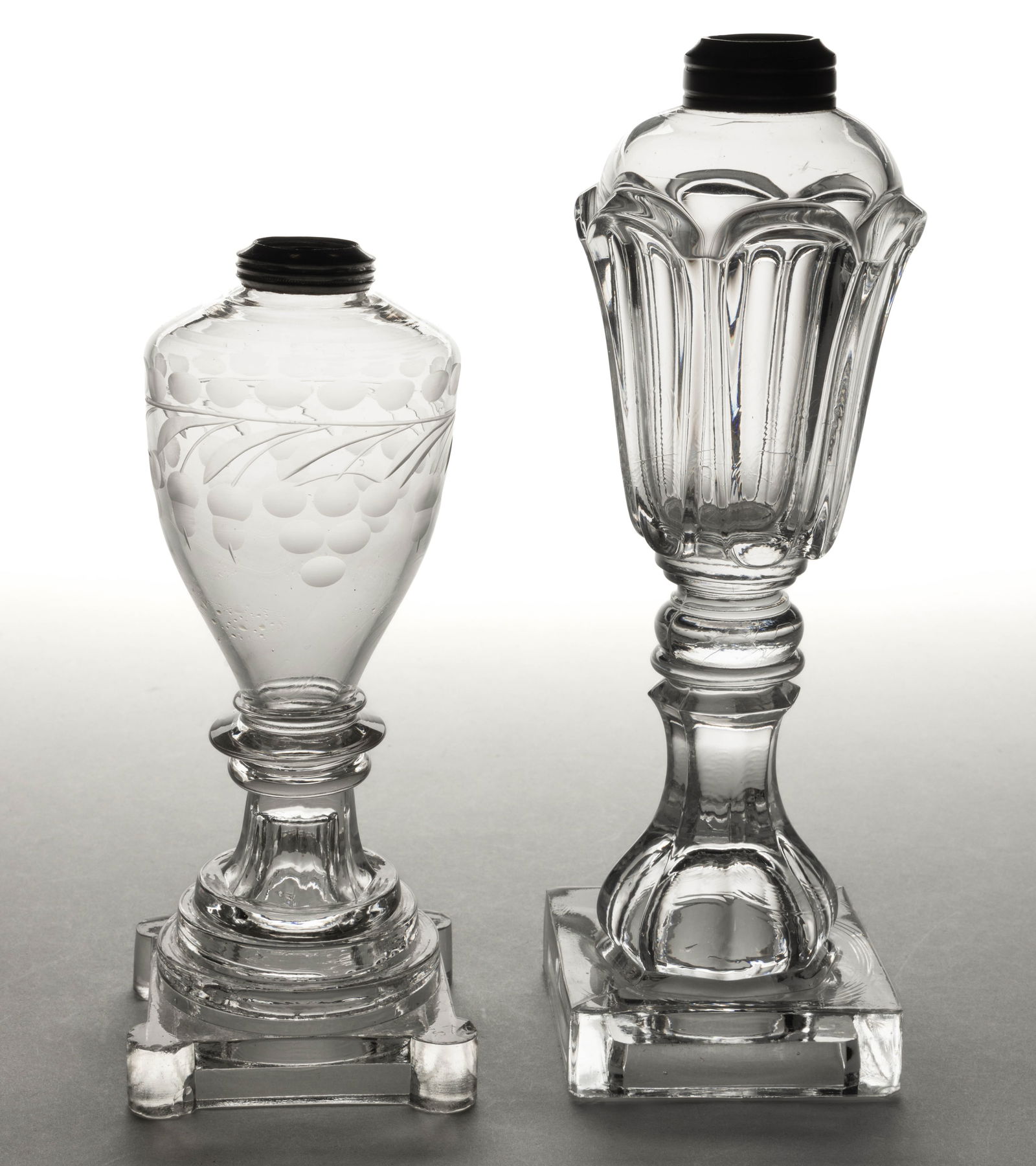 ASSORTED FREE-BLOWN AND / OR PRESSED WHALE OIL / FLUID STAND LAMPS, LOT OF TWO: ASSORTED FREE-BLOWN AND / OR PRESSED WHALE OIL / FLUID STAND LAMPS, LOT OF TWO, colorless, comprising a free-blown urn-form font with acorn and grape engraving, on a pressed stepped base with extended