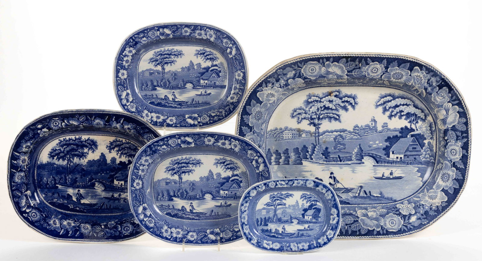 STAFFORDSHIRE BLUE TRANSFER-PRINTED WILD ROSE MOTIF CERAMIC PLATTERS, LOT OF FIVE: STAFFORDSHIRE BLUE TRANSFER-PRINTED WILD ROSE MOTIF CERAMIC PLATTERS, LOT OF FIVE, each of ovoid form and depicting Nuneham Courtenay featuring a cottage, bridge, and figures in boats in foreground wi