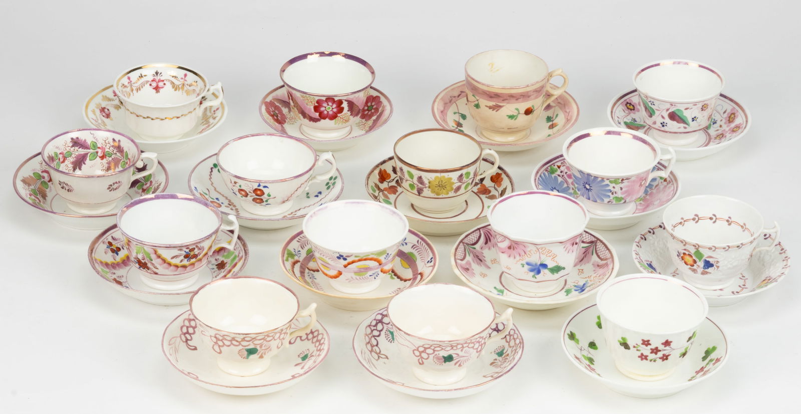 BRITISH HAND-PAINTED CERAMIC FLORAL MOTIF CUP AND SAUCER SETS, LOT OF 15: BRITISH HAND-PAINTED CERAMIC FLORAL MOTIF CUP AND SAUCER SETS, LOT OF 15, each having polychrome decorations with pink lustre accents, including one set with large alternating pink and blue flowers, o