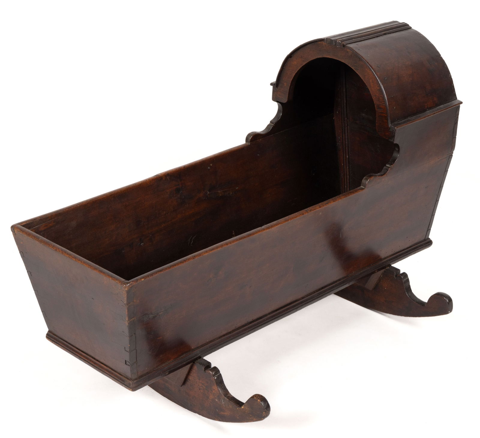 AMERICAN OR ENGLISH WALNUT HOODED CRADLE: AMERICAN OR ENGLISH WALNUT HOODED CRADLE, nailed and dovetailed construction, featuring a hooded upper section with applied decorative molding over an open well, the whole raised on shaped rockers.