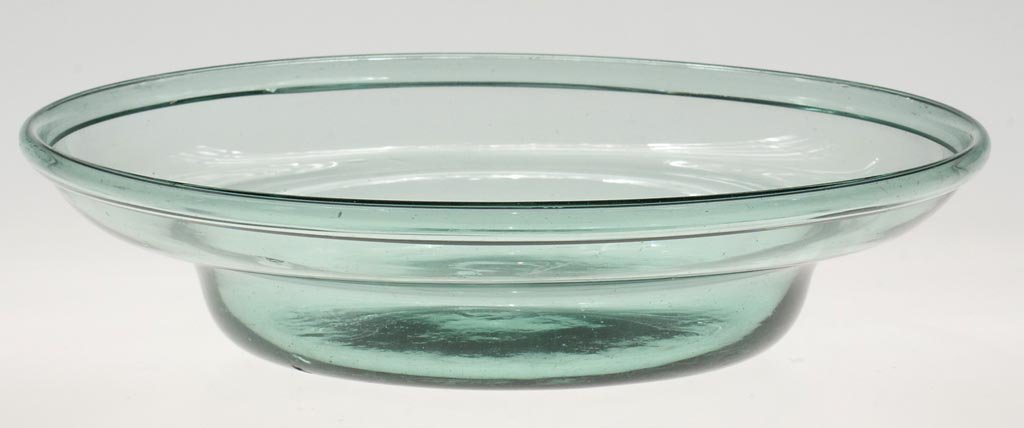 FREE-BLOWN LOW MILK PAN: FREE-BLOWN LOW MILK PAN, light green, wide ogee-shoulder form with folded rim, slight kick-up base with rough pontil mark. Probably Pittsburgh area. 1800-1850. 2 1/2" H, 10 3/4" D. Literature: Innes -