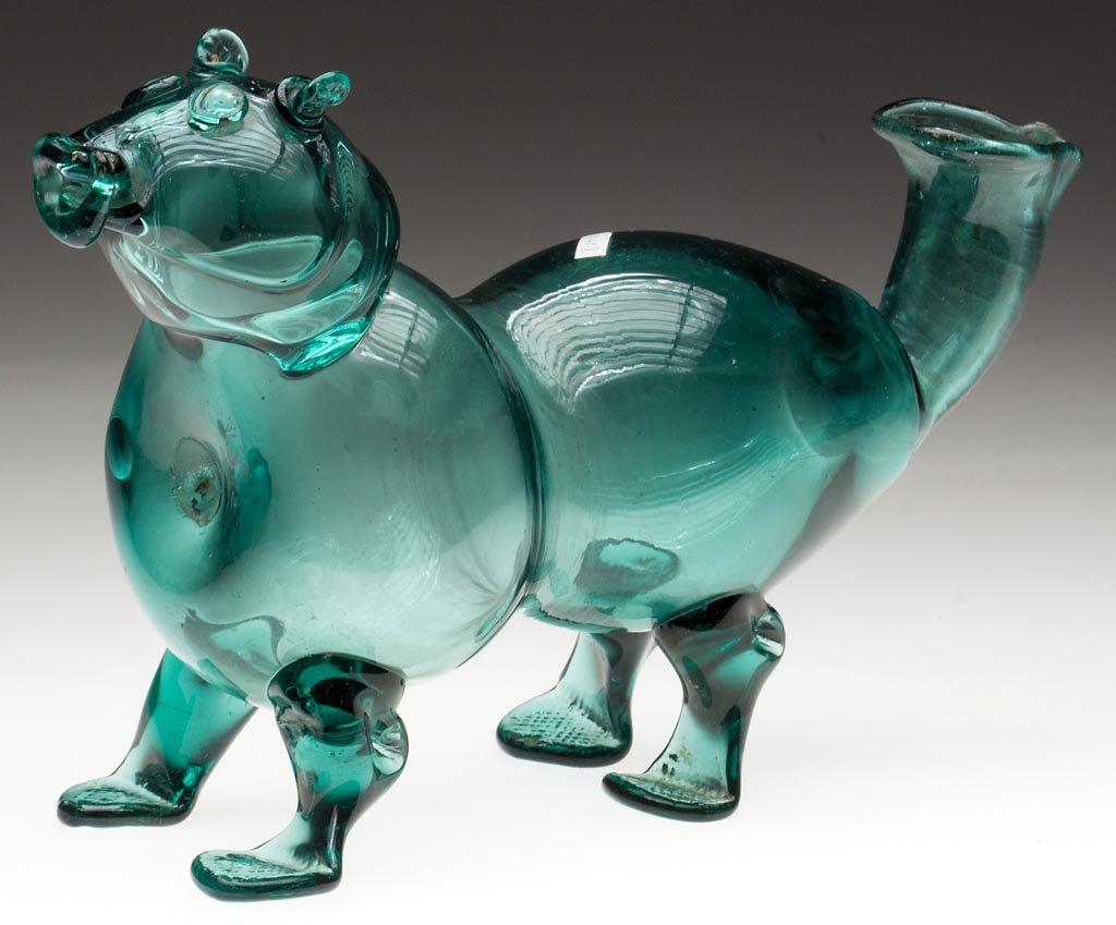 FREE-BLOWN DOG-SHAPED DRINKING BOTTLE: FREE-BLOWN DOG-SHAPED DRINKING BOTTLE, blue-green bottle glass, hollow body and head with applied facial features, four legs and open upturned tail, rough pontil mark to front under head. Possibly Cas