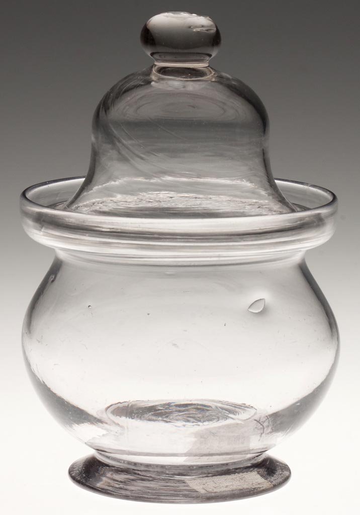 FREE-BLOWN SUGAR BOWL AND COVER: FREE-BLOWN SUGAR BOWL AND COVER, colorless, bowl with slight gray tint, compressed globular form with deep-galleried rim, raised on an applied flared foot with rough pontil mark, ogee-form cover with 