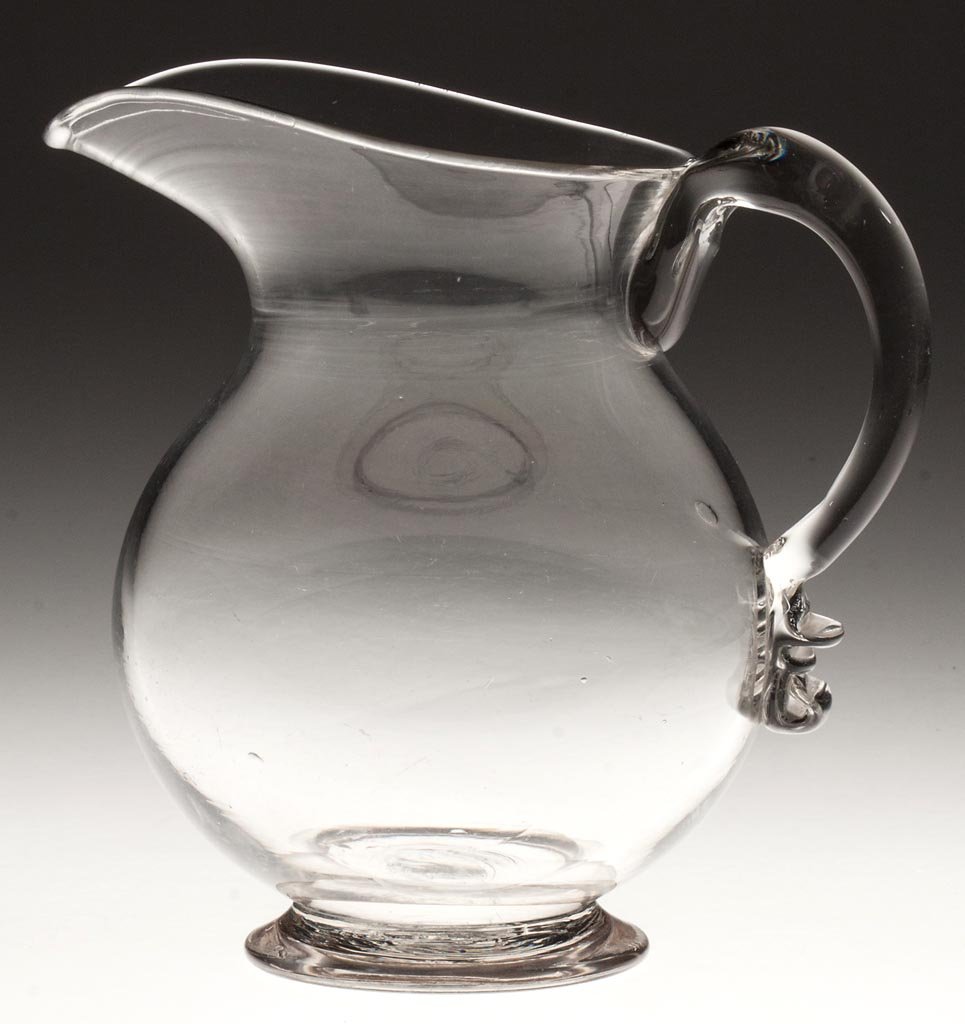 FREE-BLOWN QUART FOOTED PITCHER: FREE-BLOWN QUART FOOTED PITCHER, colorless, globular form with applied solid handle and thick, flared foot with rough pontil mark. Probably New England. 1810-1840. 7" HOA, 4 1/2" D rim, 3 1/4" D foot.