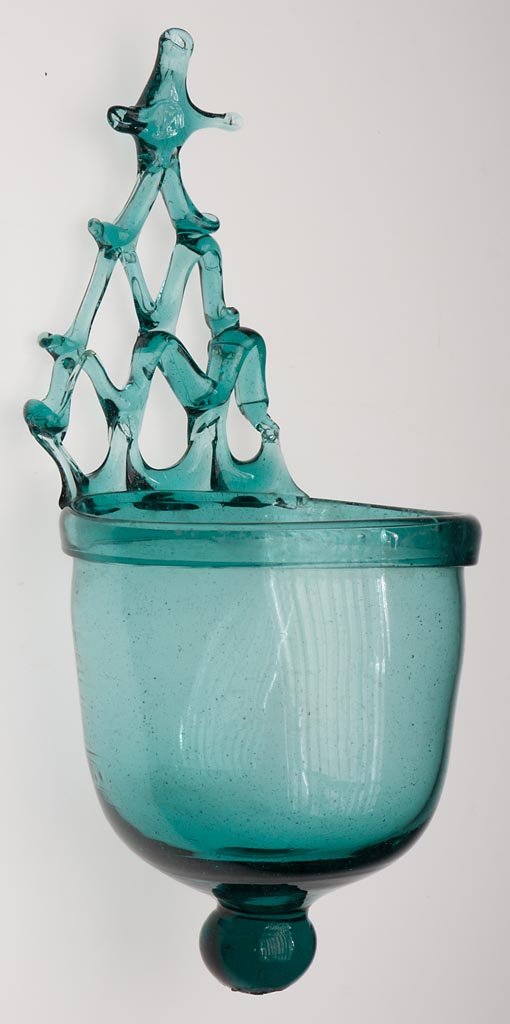 FREE-BLOWN HOLY WATER FONT: FREE-BLOWN HOLY WATER FONT, blue-green bottle glass, wall style, font with folded rim and knop extension below, applied open lattice-work back, rough pontil mark to knop. 18th or 19th century. 10 1/2"