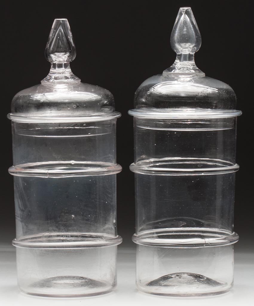 FREE-BLOWN RING JARS, NEAR MATCHING PAIR: FREE-BLOWN RING JARS, NEAR MATCHING PAIR, colorless, each of cylindrical form with two applied rings, domed cover with applied pyriform teared finial, rough pontil marks. Bakewell, Pears & Co. and oth
