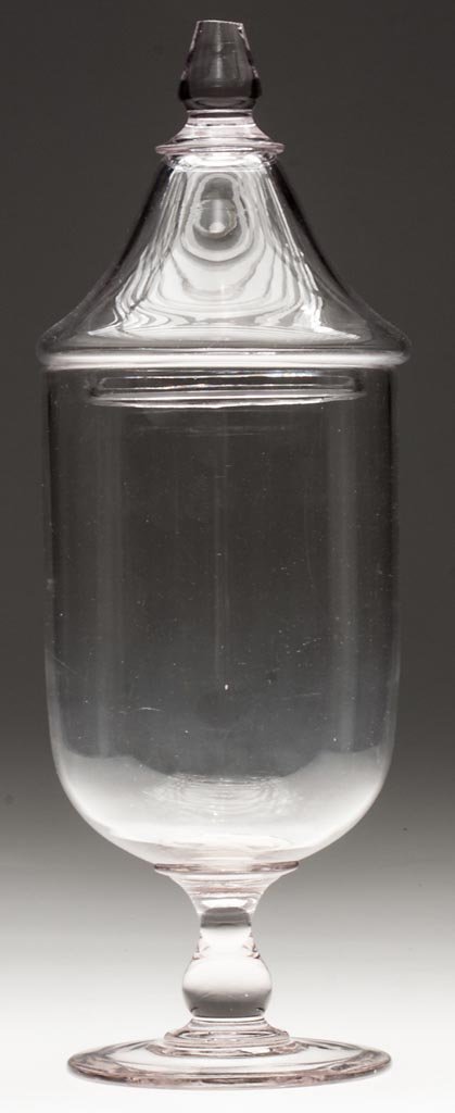 FREE-BLOWN APOTHECARY OR SHOW JAR: FREE-BLOWN APOTHECARY OR SHOW JAR, colorless, deep urn-form bowl raised on a solid, baluster stem and circular foot with polished pontil mark, peaked cover with applied, solid finial. Bakewell, Pears 