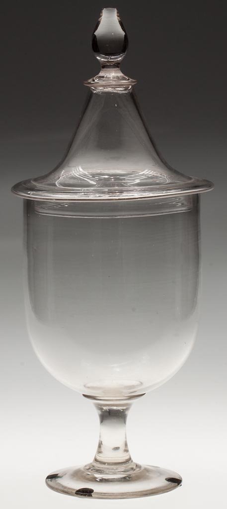 FREE-BLOWN APOTHECARY OR SHOW JAR: FREE-BLOWN APOTHECARY OR SHOW JAR, colorless, deep urn-form bowl raised on a solid stem and circular foot with polished pontil mark, peaked cover with applied, solid pyriform finial. Second half 19th 