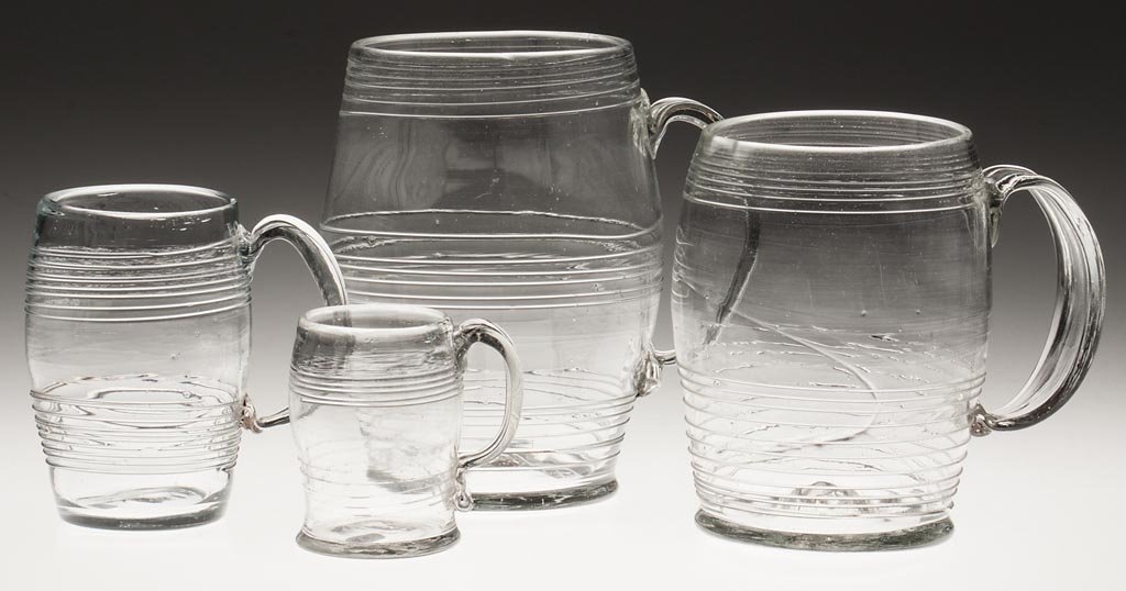Free-Blown Thread-Decorated Mugs / Cans, Graduated Set: FREE-BLOWN THREAD-DECORATED MUGS / CANS, GRADUATED SET OF FOUR, colorless, each of barrel-form with applied strap handle, one with medial rib, rough pontil marks. Probably Europe, possibly Henry Willi