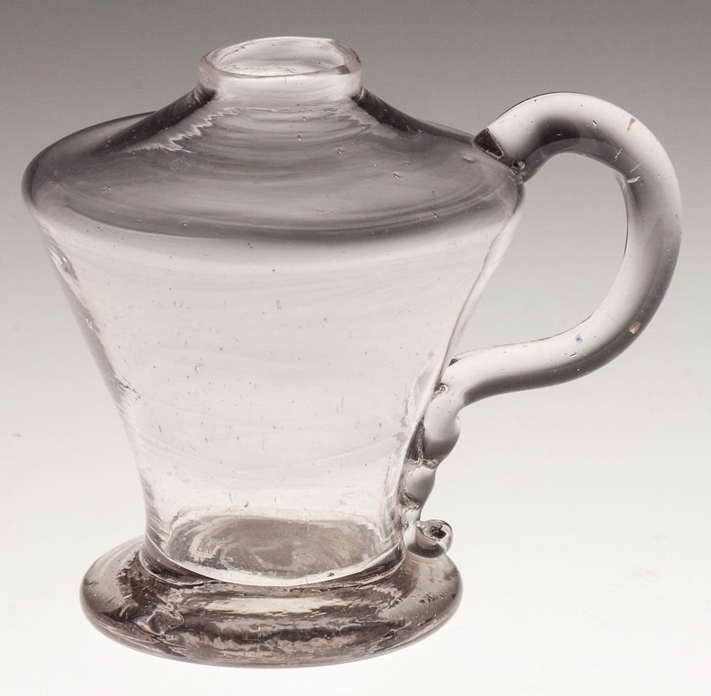FREE-BLOWN HAND LAMP: FREE-BLOWN HAND LAMP, colorless, squat conical font raised on a drawn, flared foot, applied solid handle, rough pontil mark. United States. 1820-1840. 3 1/4" H, 2 1/4" D foot. Provenance: Collection o