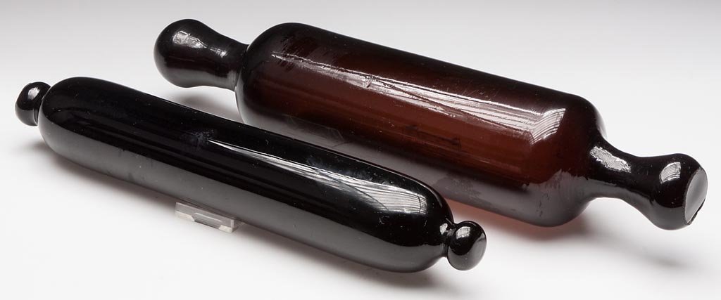 FREE-BLOWN ROLLING PINS, LOT OF TWO: FREE-BLOWN ROLLING PINS, LOT OF TWO, comprising a deep amber example with drawn handles and a deep amethyst example with knob handles, each with rough pontil marks. Second half 19th century. 14 1/4" a