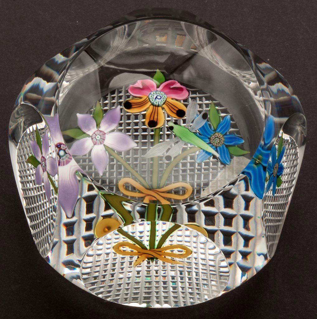 PERTHSHIRE BOUQUET AND DRAGONFLY FACETTED PAPERWEIGHT: PERTHSHIRE BOUQUET AND DRAGONFLY FACETTED PAPERWEIGHT, featuring three long-stem flowers tied with a yellow ribbon, one with a center "P" cane, and a hovering green dragonfly, crosshatch-cut base with