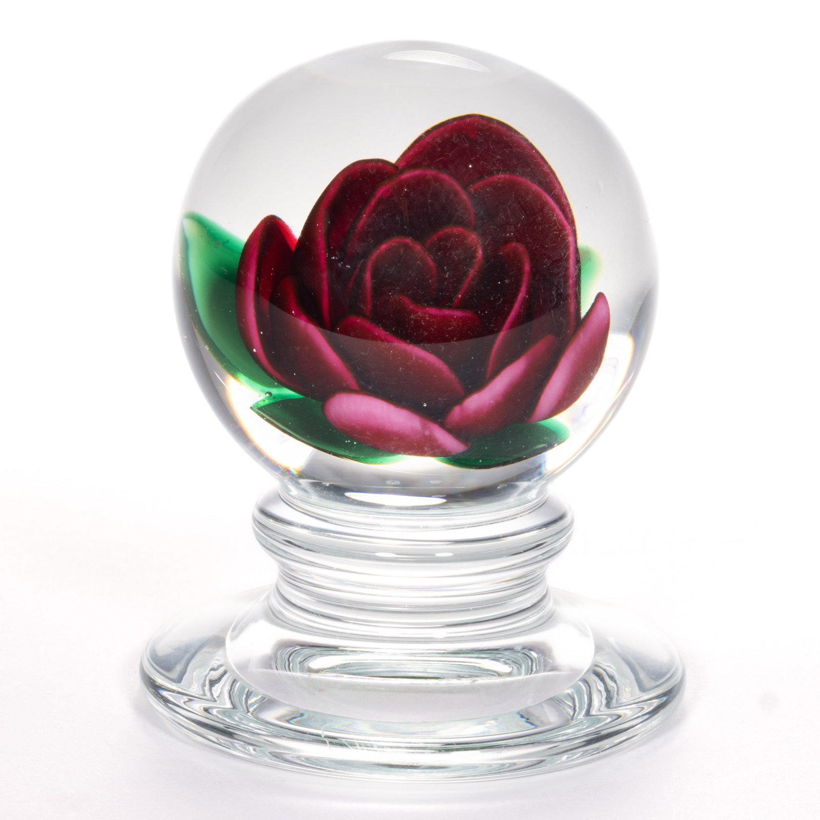 CHARLES KAZIUN JR. (AMERICAN, 1919-1992) CRIMP ROSE LAMPWORK STUDIO ART GLASS PEDESTAL PAPERWEIGHT: CHARLES KAZIUN JR. (AMERICAN, 1919-1992) CRIMP ROSE LAMPWORK STUDIO ART GLASS PEDESTAL PAPERWEIGHT, fuchsia crimp rose with four protruding green leaves, signature cane to the underside, raised o